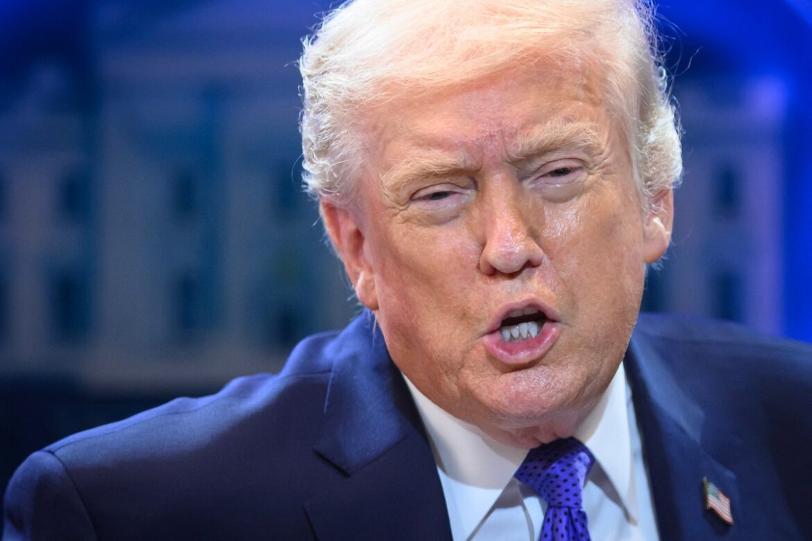 Former President Donald Trump speaking during an event, showcasing his signature hairstyle and wearing a dark suit with a blue shirt and purple tie.