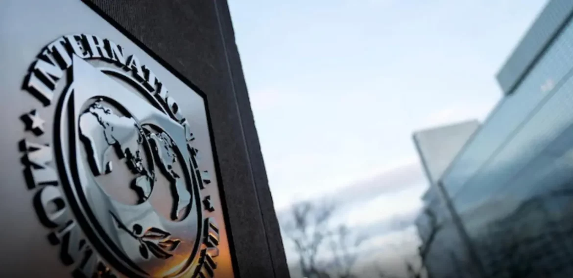 Close-up of the International Monetary Fund (IMF) emblem on a building facade, with a blurred modern glass structure in the background, symbolizing global financial governance and economic stability.