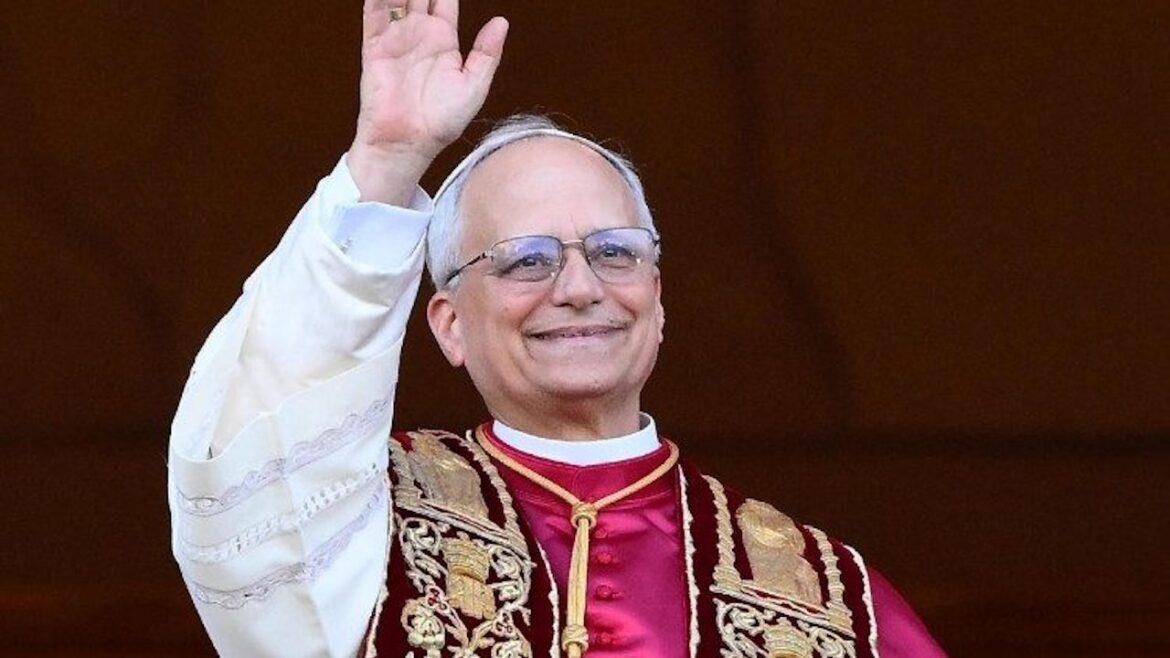 Pope Francis smiling and waving from a balcony, dressed in ornate red and white papal robes, during a public appearance.