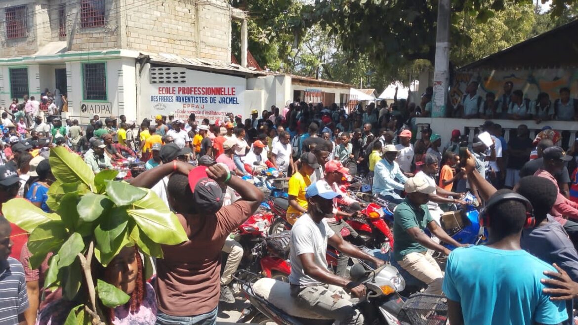 Crowd gathered outside a professional school in Jacmel, Haiti, with people on motorcycles and a vibrant atmosphere. The scene showcases a community event, highlighting local engagement and cultural participation.